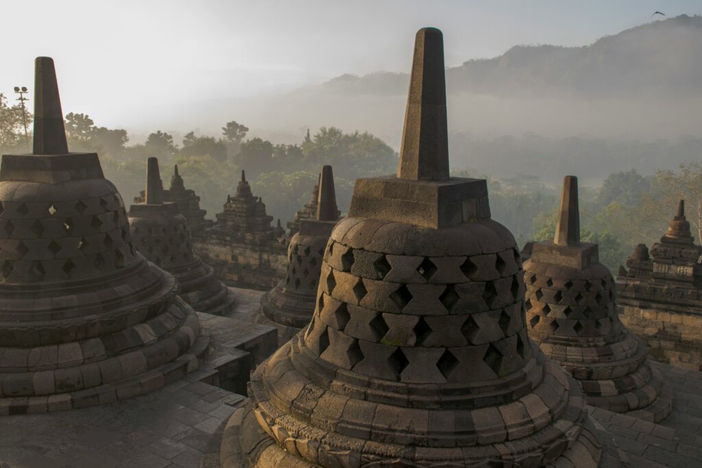 Borobudur Temple shrouded in mist and surrounded by clouds, creating a mystical and serene atmosphere with its iconic stupas barely visible through the fog.