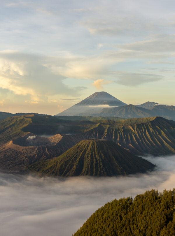 View of Mount Bromo with its mist-covered base, surrounded by a vast plain and a clear sky with a few clouds, creating a dramatic yet serene atmosphere.