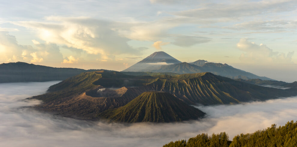 View of Mount Bromo with its mist-covered base, surrounded by a vast plain and a clear sky with a few clouds, creating a dramatic yet serene atmosphere.