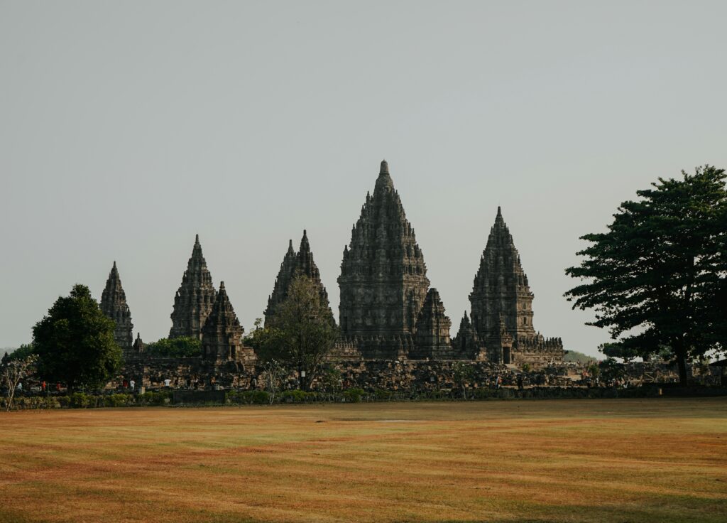 The majestic Prambanan Temple complex, featuring towering Hindu temples with intricate stone carvings, set against a clear blue sky and lush green surroundings.