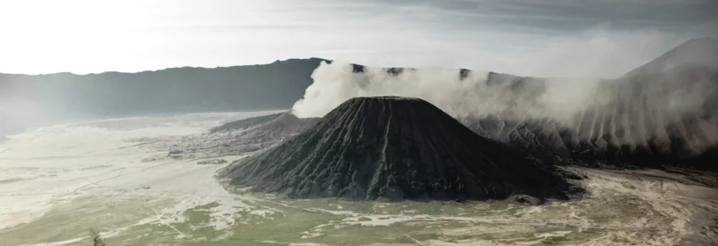 Misty sunrise view of Mount Bromo with smoking crater and surrounding mountains in East Java, Indonesia