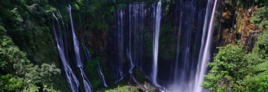Aerial view of Tumpak Sewu Waterfall cascading in a semicircle surrounded by lush jungle in East Java, Indonesia